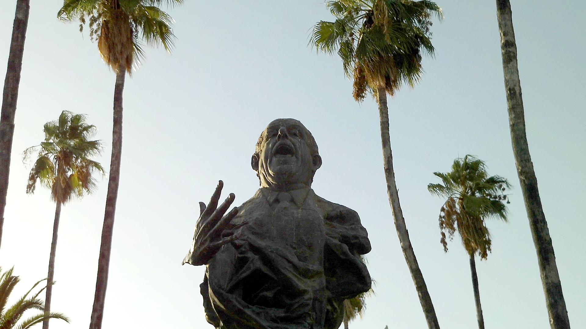 Busto de Antonio Mairena visto desde abajo, con palmeras y cielo al fondo