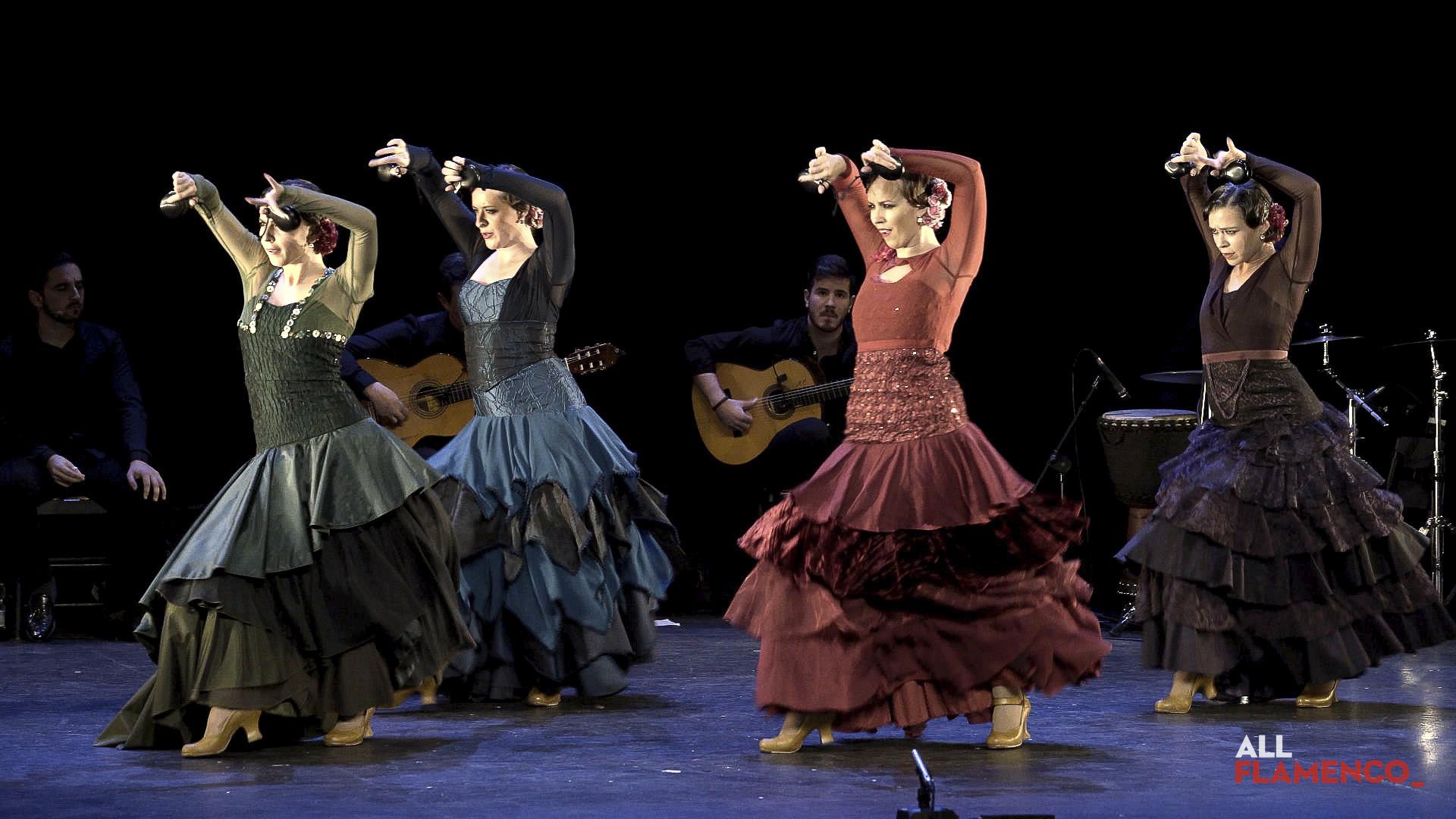 Cuatro bailaoras con los brazos en alto y las castañuelas en las manos, con vestidos de volantes de colores