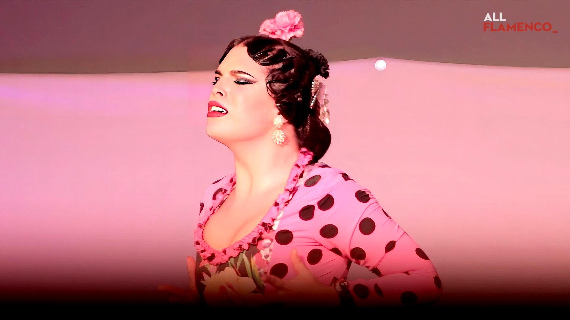 A bailaora in profile in a pink polka-dot dress against a luminous pink background