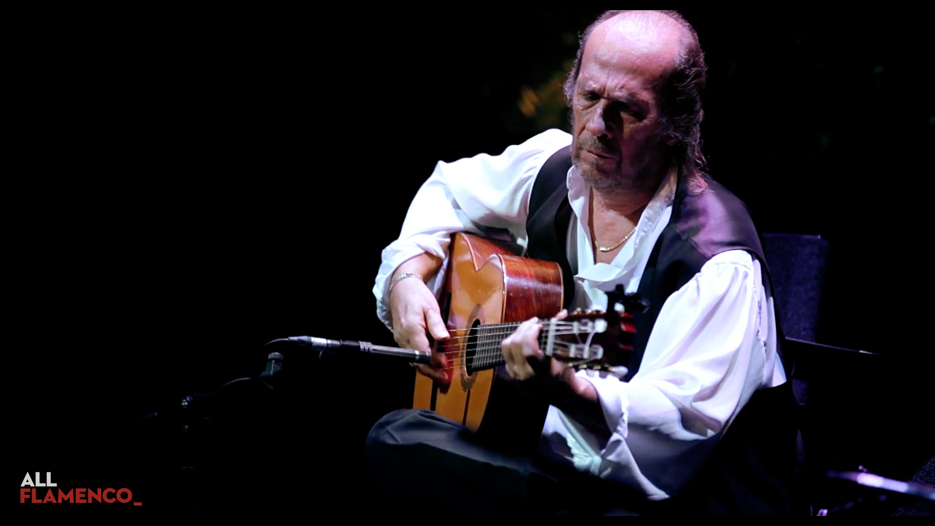 Paco de Lucía tocando la guitarra sentado, con camisa blanca y chaleco
