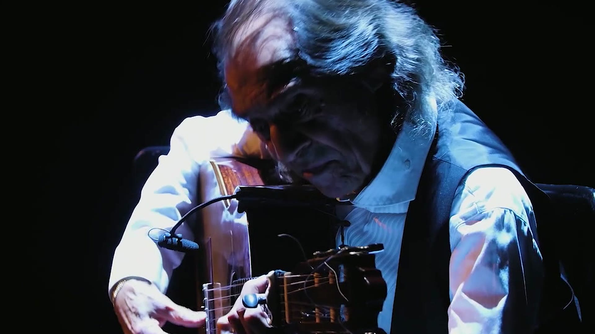 Pepe Habichuela a la guitarra en el Teatro Cervantes Primer plano de Pepe Habichuela tocando la guitarra flamenca, iluminado por un foco sobre fondo negro, en el Teatro Cervantes de Málaga