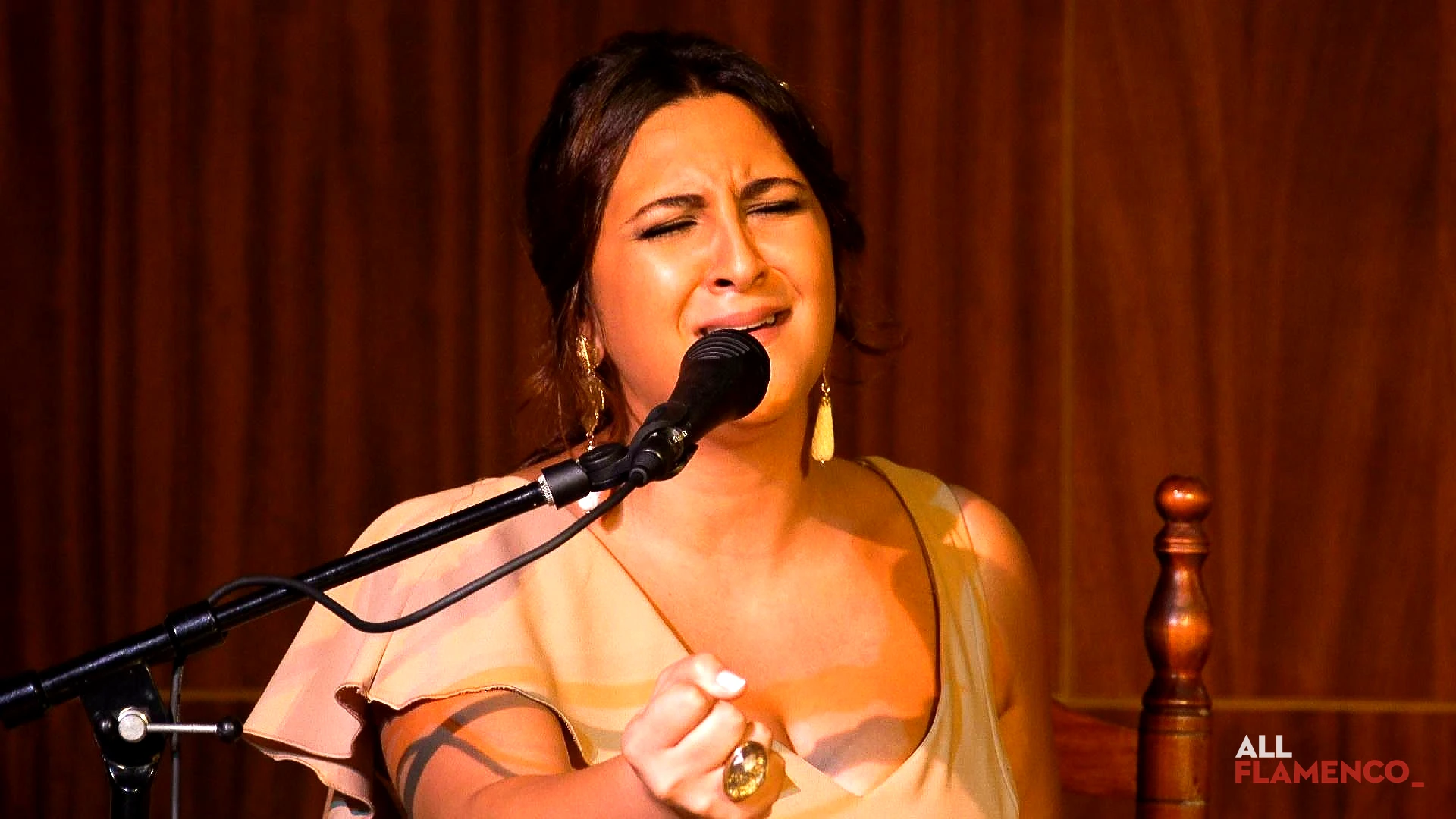 Una cantaora flamenca en primer plano, con los ojos cerrados y la boca abierta, cantando ante el micrófono