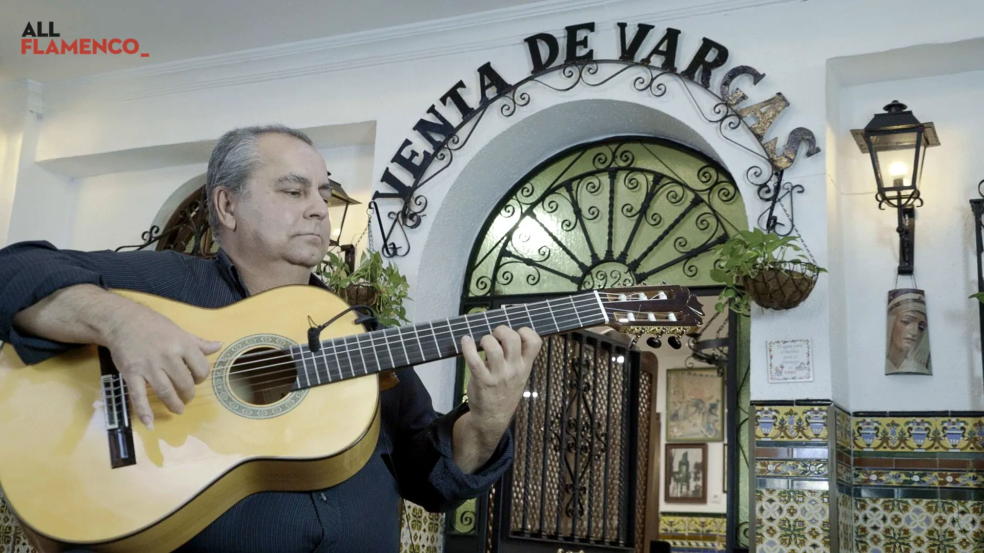 Un guitarrista toca sentado en la puerta encalada de la Venta de Vargas, entre azulejos y un farol