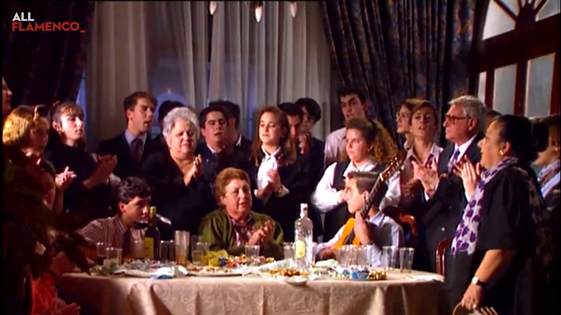 Una familia canta y toca palmas alrededor de una mesa, con pandereta y guitarra