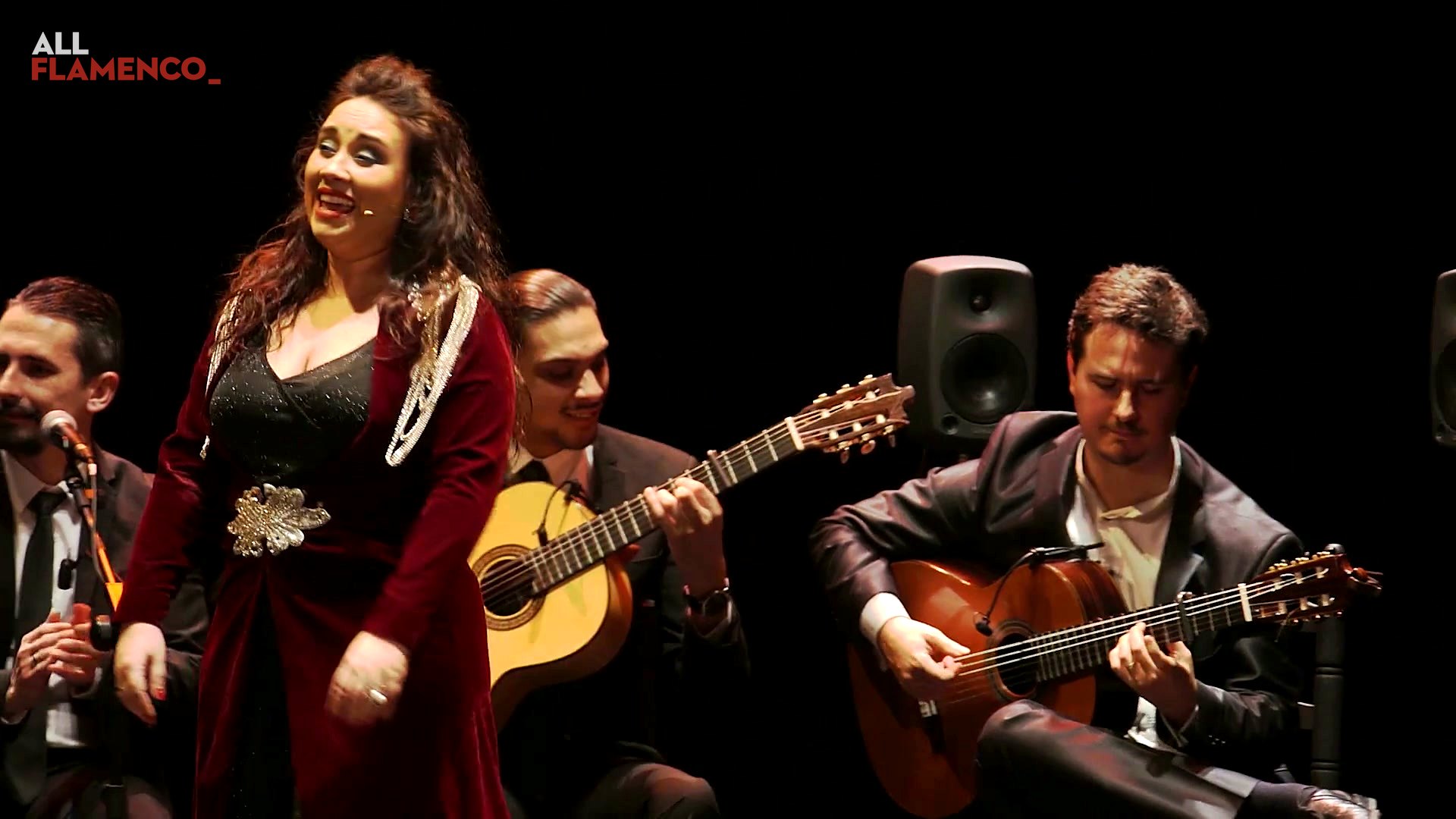 Encarna Anillo, dressed in red, sings smiling between two guitarists in «Cádiz, corazón de mar»