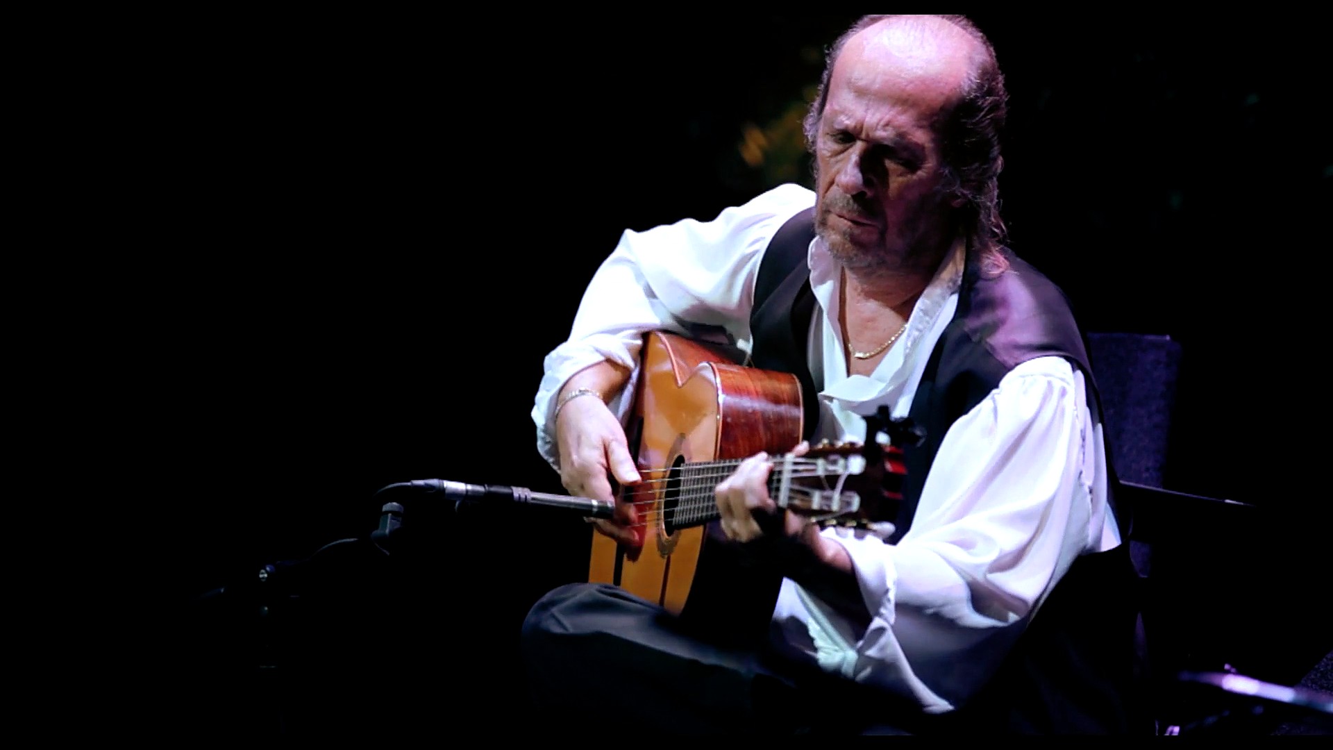 Paco de Lucía tocando la guitarra sentado, con camisa blanca y chaleco